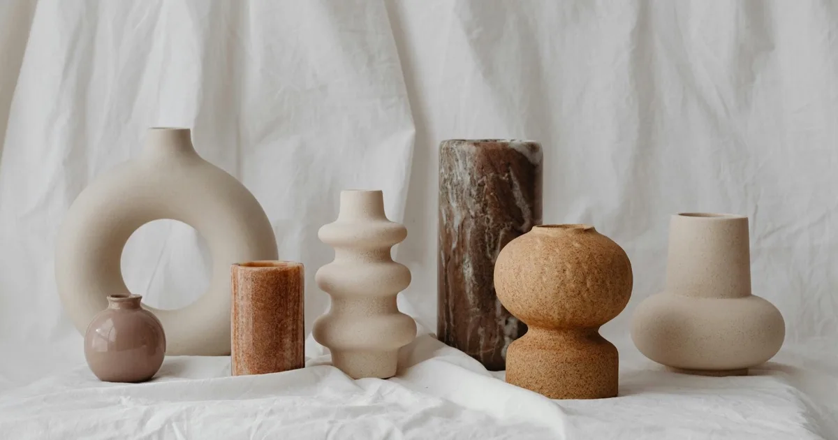 Collection of handcrafted ceramic vases in neutral tones arranged on a wooden shelf with dried flowers